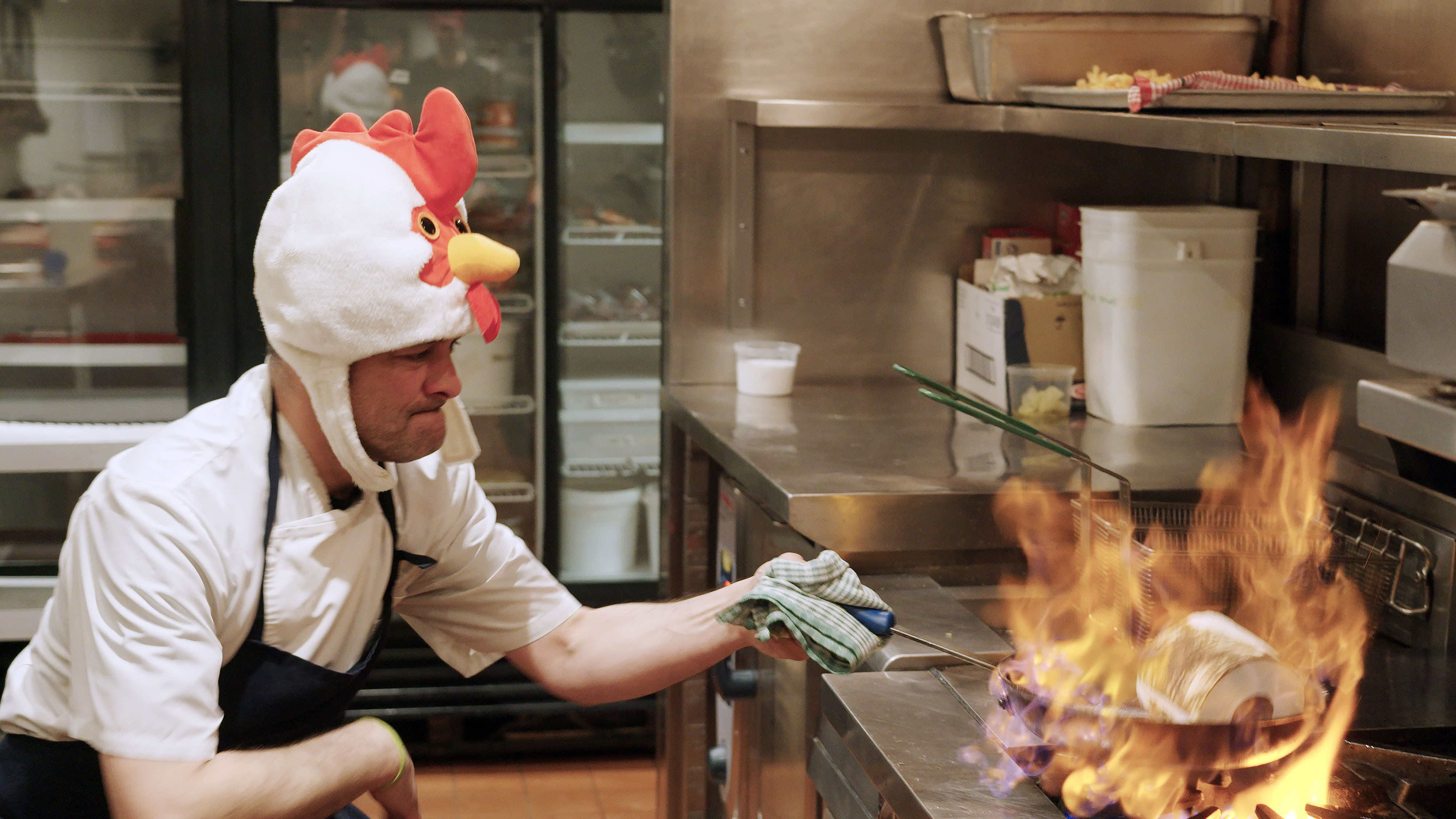 Charles-Antoine Crête en costume de poulet cuisine avec des flammes.